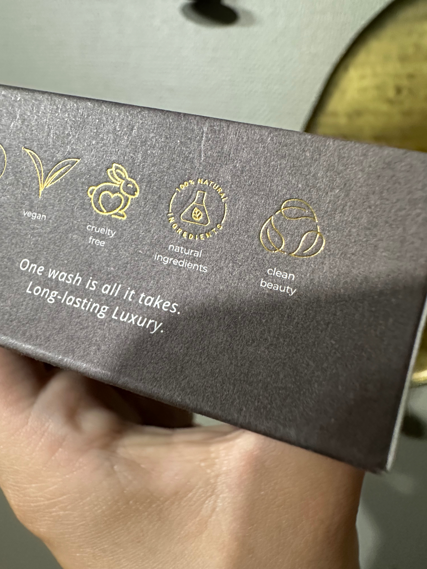 Mörk kartong med guldtryckta symboler för vegan, cruelty free, 100% natural ingredients och clean beauty, symboler som inte längre får användas.